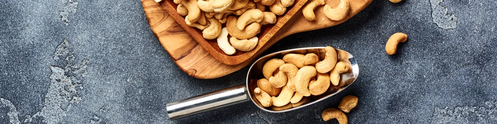 cashew nuts in a silver scoop next to a wooden serving board